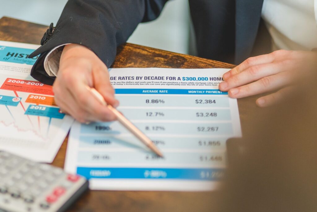 Hand with a pencil pointing at a printed table of mortgage rates and monthly payments