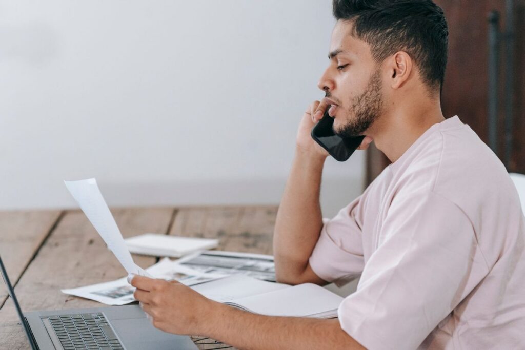 Man on the phone at a table with loan papers and a laptop