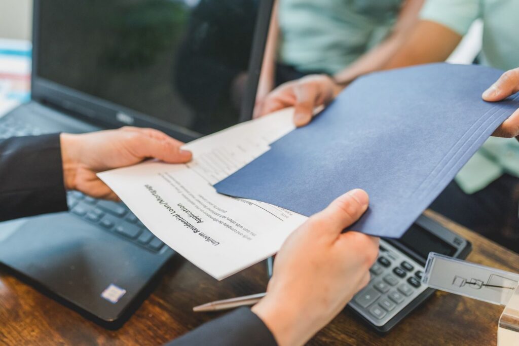 Two people passing loan documents in a blue folder over a desk