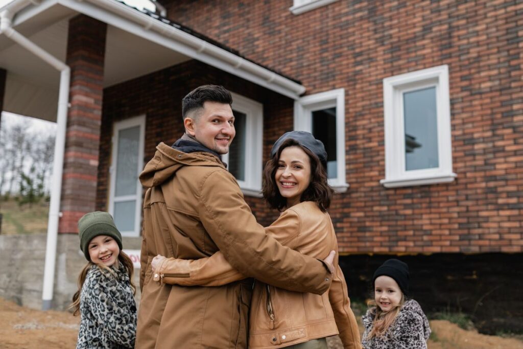 Family of four hugging in front of their new brick home