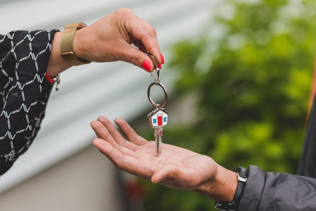 Hand passing a house key with a small house keychain to a new owner