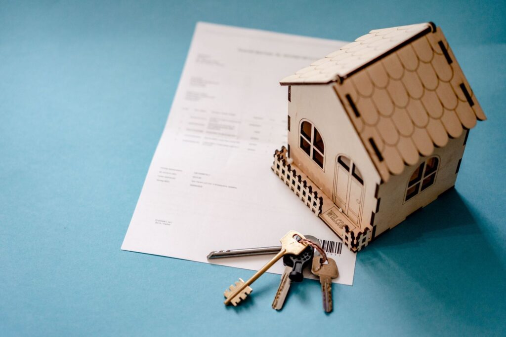 Small wooden house model and a set of keys lying on a contract