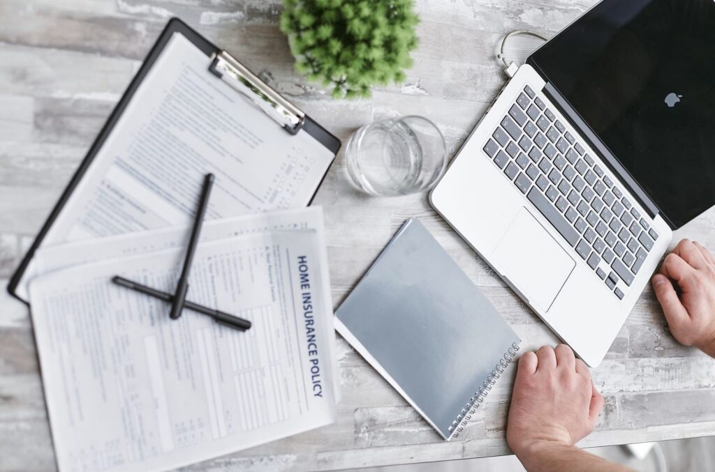 Insurance policy, forms on a clipboard and a laptop laid out on a desk