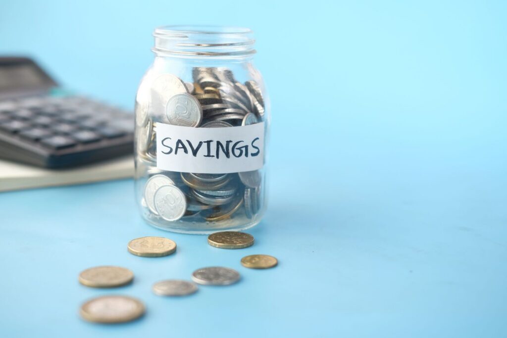 Glass jar labeled Savings filled with coins next to a calculator